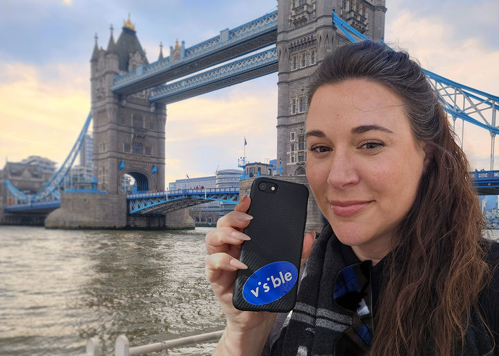 Women holding a Visible phone next to the Tower Bridge