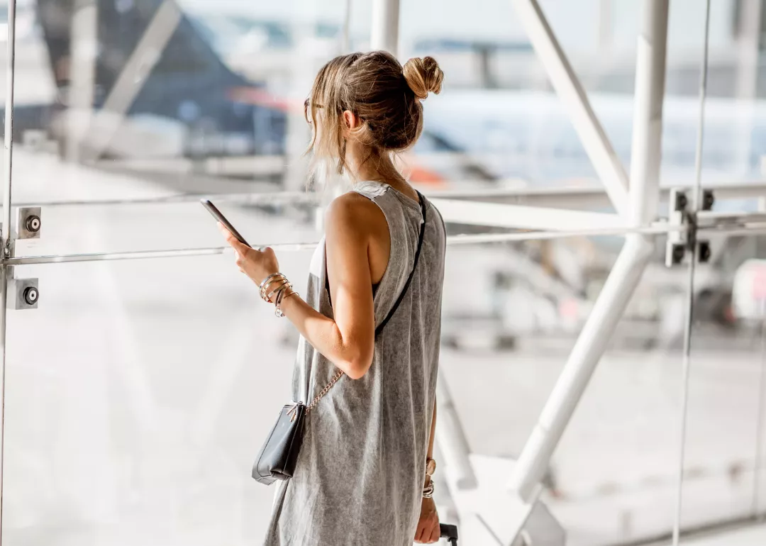 A woman holding a phone, looking out the window of the airport