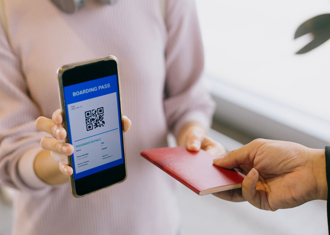 A person holding up a phone with a mobile boarding pass, handing someone a passport