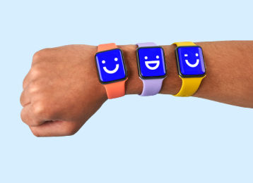 wrist with three smartwatches displaying emojis